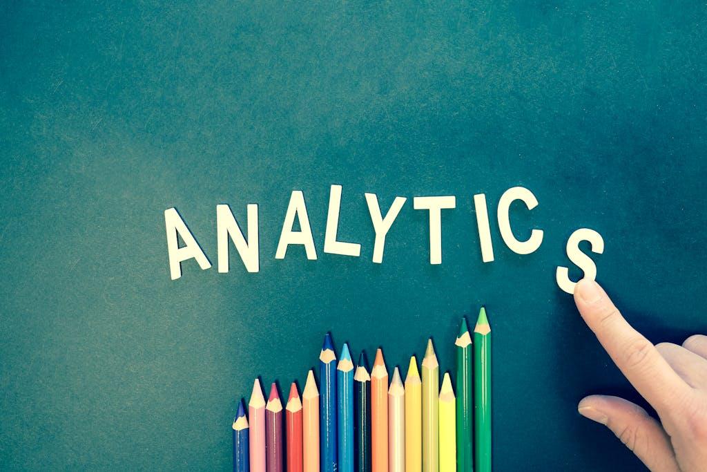 The word ANALYTICS above a row of coloring pencils with an index finger pointing at the last letter