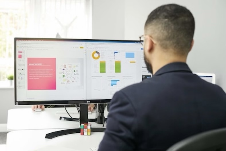 A person sitting facing a wide computer monitor displaying SEO-related graphics