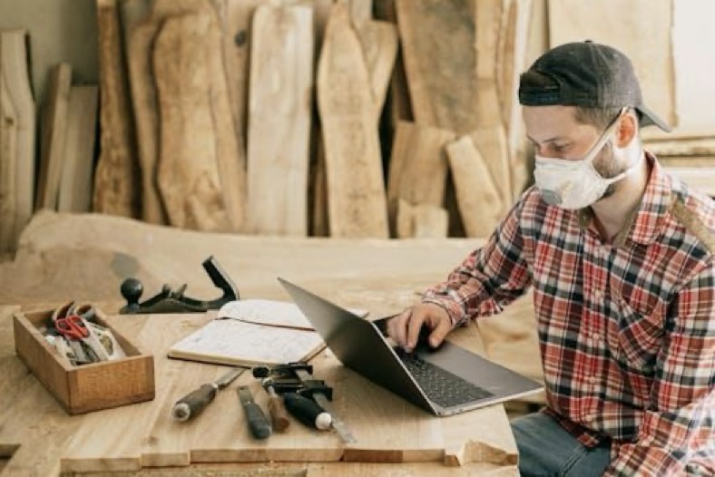 Man using a laptop surrounded by carpentry tools at a wood workshop