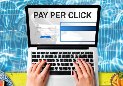 A laptop monitor showing the words Pay Per Click paid ad cost against a watery background with a person's hands on the keyboard